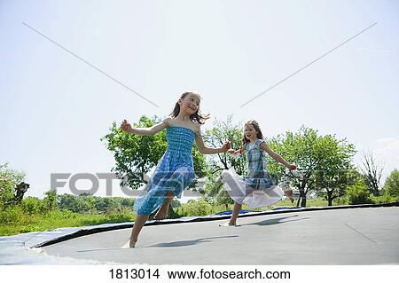 Playful, carefree barefoot girls in dresses playing on trampoline in sunny backyard View Large Photo Image Picture - Playful, carefree barefoot girls in dresses playing on trampoline in sunny backyard. Fotosearch