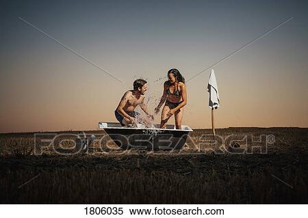 Stock Photography - Playful couple splashing in bathtub in rural field. Fotosearch