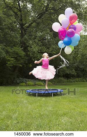Playful girl jumping on trampoline while holding balloons at backyard View Large Photo Image Stock Photograph - Playful girl jumping on trampoline while holding balloons at backyard. Fotosearch