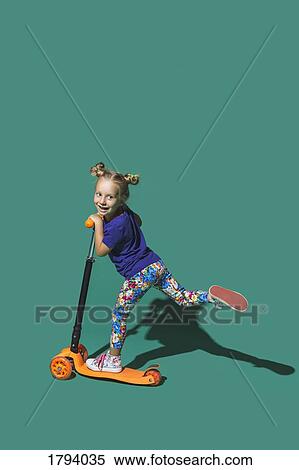 Playful girl riding scoter on green background View Large Photo Image Stock Photography - Playful girl riding scoter on green background. Fotosearch