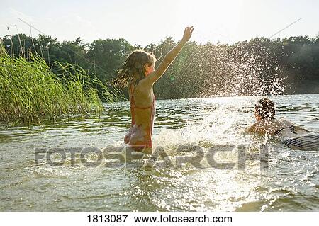 Playful girl splashing and woman swimming in sunny summer lake View Large Photo Image Stock Photo - Playful girl splashing and woman swimming in sunny summer lake. Fotosearch