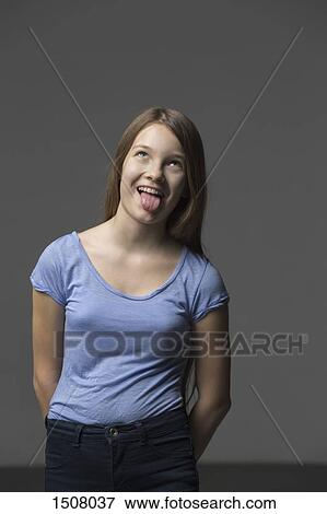 Playful girl sticking out tongue while standing against gray background View Large Photo Image Stock Photo - Playful girl sticking out tongue while standing against gray background. Fotosearch