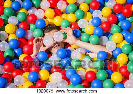 Stock Photography - Playful young man laying in multicolor ball pool. Fotosearch