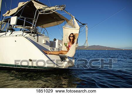 Stock Photo - Portrait carefree woman relaxing with cocktail in hammock on yacht over sunny ocean. Fotosearch
