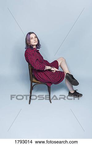 Portrait confident and fashionable young woman sitting on chair against blue background View Large Photo Image Picture - Portrait confident and fashionable young woman sitting on chair against blue background. Fotosearch