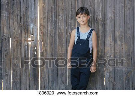 Portrait confident boy in overalls at wooden fence View Large Photo Image Stock Image - Portrait confident boy in overalls at wooden fence. Fotosearch