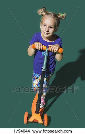 Portrait confident girl riding scooter against green background View Large Photo Image Picture - Portrait confident girl riding scooter against green background. Fotosearch