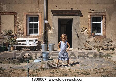Stock Photo - Portrait confident girl standing in front of sunny farmhouse. Fotosearch