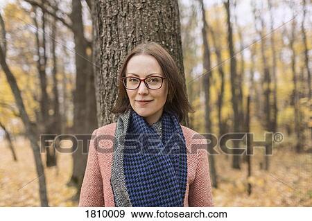 Stock Photo - Portrait confident woman in scarf standing against tree in autumn park. Fotosearch