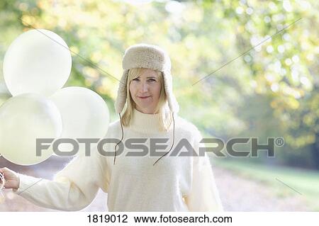 Portrait confident woman in white fur hat holding bunch of balloons in park View Large Photo Image Stock Image - Portrait confident woman in white fur hat holding bunch of balloons in park. Fotosearch