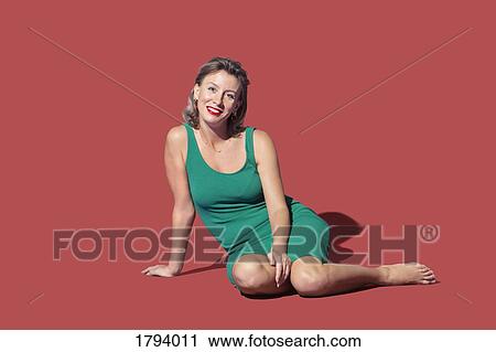 Stock Image - Portrait confident woman sitting on red background. Fotosearch