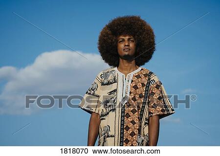 Portrait confident young man with afro standing against blue sky with clouds View Large Photo Image Stock Image - Portrait confident young man with afro standing against blue sky with clouds. Fotosearch