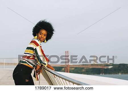 Portrait confident young woman at waterfront with 25 de Abril Bridge in background, Lisbon, Portugal View Large Photo Image Stock Photo - Portrait confident young woman at waterfront with 25 de Abril Bridge in background, Lisbon, Portugal. Fotosearch