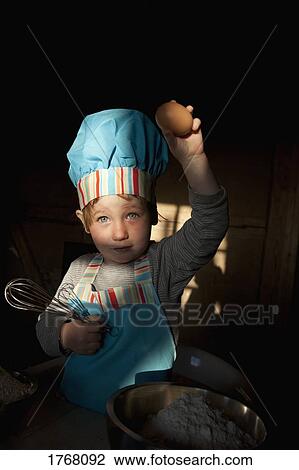 Stock Image - Portrait cute girl in chefs hat baking, holding egg. Fotosearch