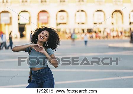 Stock Photography - Portrait enthusiastic young woman forming heart-shape with hands in Praca do Comercio, Lisbon. Fotosearch