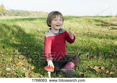 Stock Image - Portrait happy girl sitting next to mushroom. Fotosearch