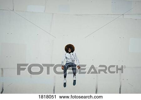 Stock Image - Portrait happy young man with afro sitting on wall. Fotosearch