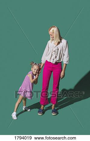 Stock Photo - Portrait mother and daughter holding hands against green background. Fotosearch
