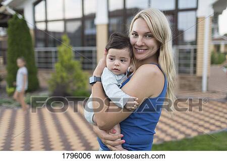 Stock Photograph - Portrait mother holding baby son in backyard. Fotosearch