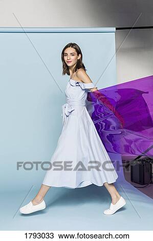 Stock Image - Portrait of a female fashion model posing with purple plastic sheet against blue background. Fotosearch