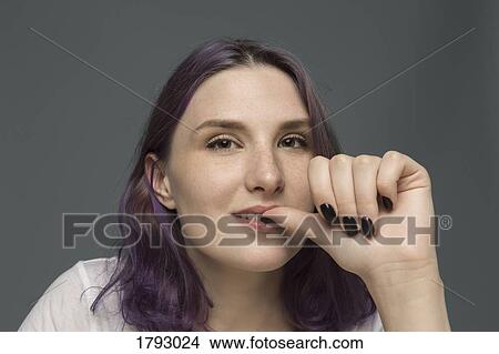 Picture - Portrait of a young woman with dyed hair biting nail against gray background. Fotosearch