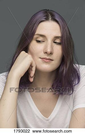 Stock Image - Portrait of a young woman with dyed hair and looking down against gray background. Fotosearch