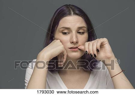 Portrait of a young woman with dyed hair biting thumb and looking down against gray background View Large Photo Image Stock Image - Portrait of a young woman with dyed hair biting thumb and looking down against gray background. Fotosearch