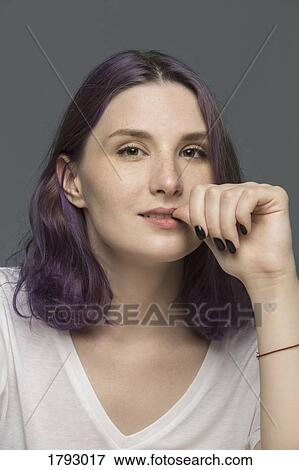 Portrait of a young woman with dyed hair biting nail against gray background View Large Photo Image Stock Photo - Portrait of a young woman with dyed hair biting nail against gray background. Fotosearch