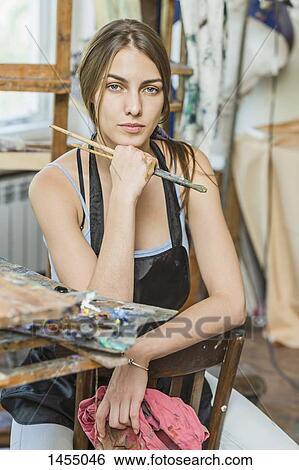 Stock Photograph - Portrait of beautiful female painter sitting on chair in studio. Fotosearch