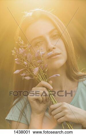 Stock Image - Portrait of beautiful woman holding flowers on sunny day. Fotosearch