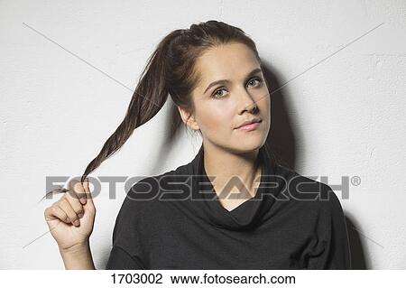 Stock Image - Portrait of beautiful woman holding ponytail against white background. Fotosearch