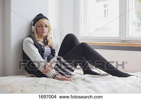 Portrait of beautiful woman listening to music through headphones while sitting on bed at home View Large Photo Image Picture - Portrait of beautiful woman listening to music through headphones while sitting on bed at home. Fotosearch