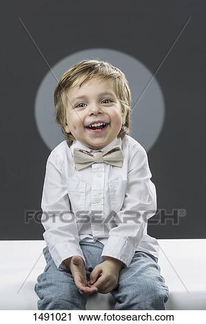 Portrait of cheerful boy with bowtie sitting against gray background View Large Photo Image Stock Image - Portrait of cheerful boy with bowtie sitting against gray background. Fotosearch