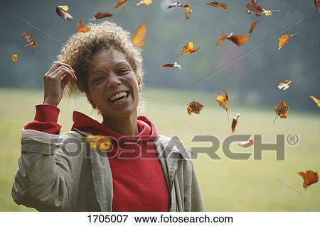 Portrait of cheerful woman with hand in hair amidst autumn leaves View Large Photo Image Stock Photo - Portrait of cheerful woman with hand in hair amidst autumn leaves. Fotosearch