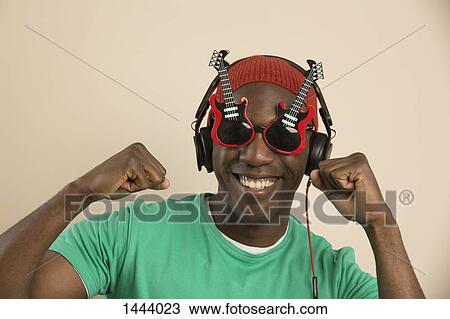 Portrait of cheerful young man wearing guitar shaped glasses and headphones View Large Photo Image Stock Image - Portrait of cheerful young man wearing guitar shaped glasses and headphones. Fotosearch