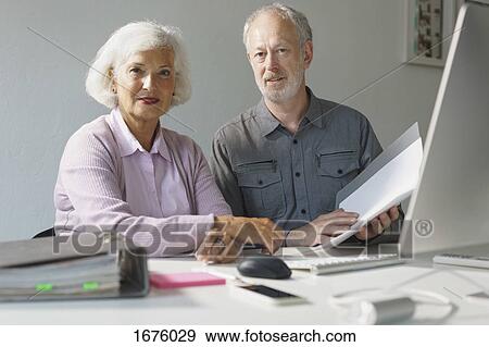 Stock Photo - Portrait of confident business colleagues with documents at desk in office. Fotosearch