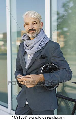 Portrait of confident businessman holding mobile phone and cycle helmet while standing against glass View Large Photo Image Stock Photo - Portrait of confident businessman holding mobile phone and cycle helmet while standing against glass. Fotosearch