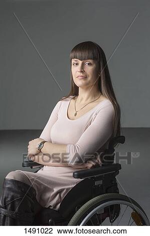 Stock Image - Portrait of confident disabled woman in wheelchair against gray background. Fotosearch