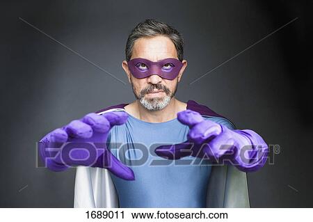 Stock Image - Portrait of confident superhero standing amidst plants against gray background. Fotosearch