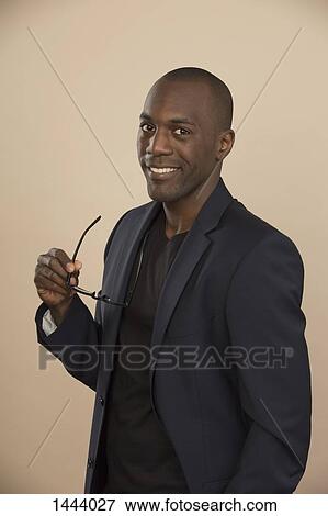 Stock Photo - Portrait of confident well-dressed man holding eyeglasses against colored background. Fotosearch