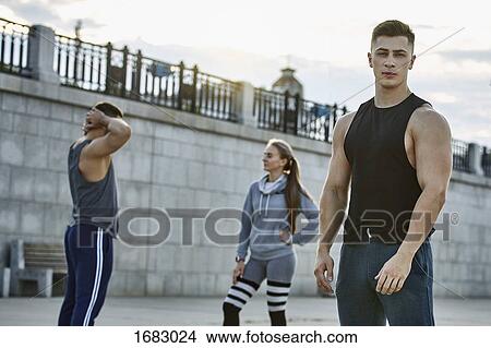 Picture - Portrait of confident young athlete standing with friends against bridge. Fotosearch