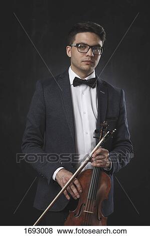 Portrait of confident young man holding violin while standing against black background View Large Photo Image Stock Photo - Portrait of confident young man holding violin while standing against black background. Fotosearch