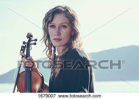 Portrait of confident young woman holding violin against clear sky on sunny day View Large Photo Image Stock Photo - Portrait of confident young woman holding violin against clear sky on sunny day. Fotosearch