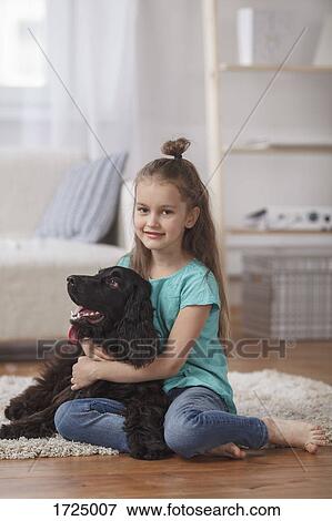 Portrait of cute girl embracing dog while sitting on rug at home View Large Photo Image Stock Photo - Portrait of cute girl embracing dog while sitting on rug at home. Fotosearch