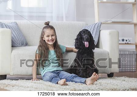 Stock Photo - Portrait of cute girl sitting by Cocker Spaniel on rug at home. Fotosearch