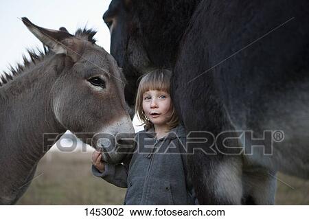 Stock Image - Portrait of cute girl standing with donkeys on field. Fotosearch