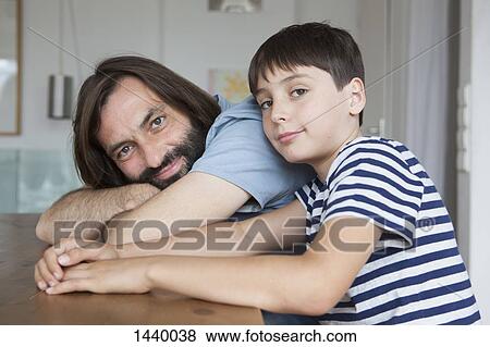 Portrait of father and son sitting at table in house View Large Photo Image Stock Photo - Portrait of father and son sitting at table in house. Fotosearch