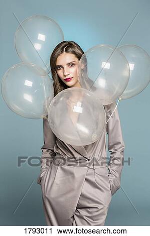 Portrait of female fashion model standing with balloons against blue background View Large Photo Image Stock Image - Portrait of female fashion model standing with balloons against blue background. Fotosearch