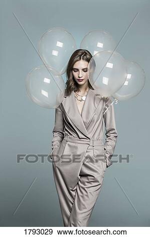 Stock Photo - Portrait of female fashion model standing with balloons against blue background. Fotosearch