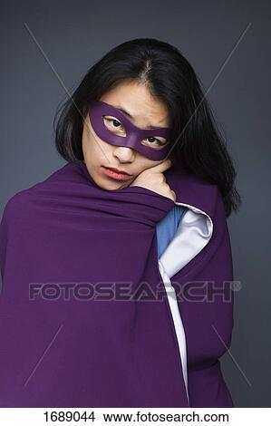 Picture - Portrait of female superhero wearing purple cape standing against gray background. Fotosearch